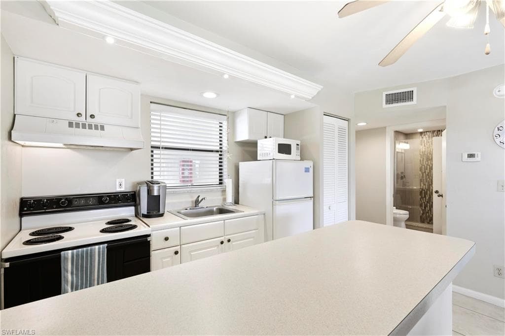 Kitchen with ceiling fan, white appliances, and white cabinetry