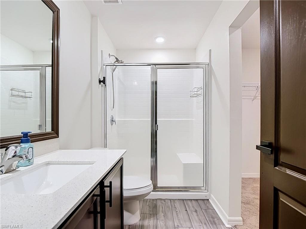 Bathroom featuring wood-finish flooring, a contemporary vanity with a white countertop and rectangular sink, a framed mirror, and a shower with sliding glass doors and white subway tile surround