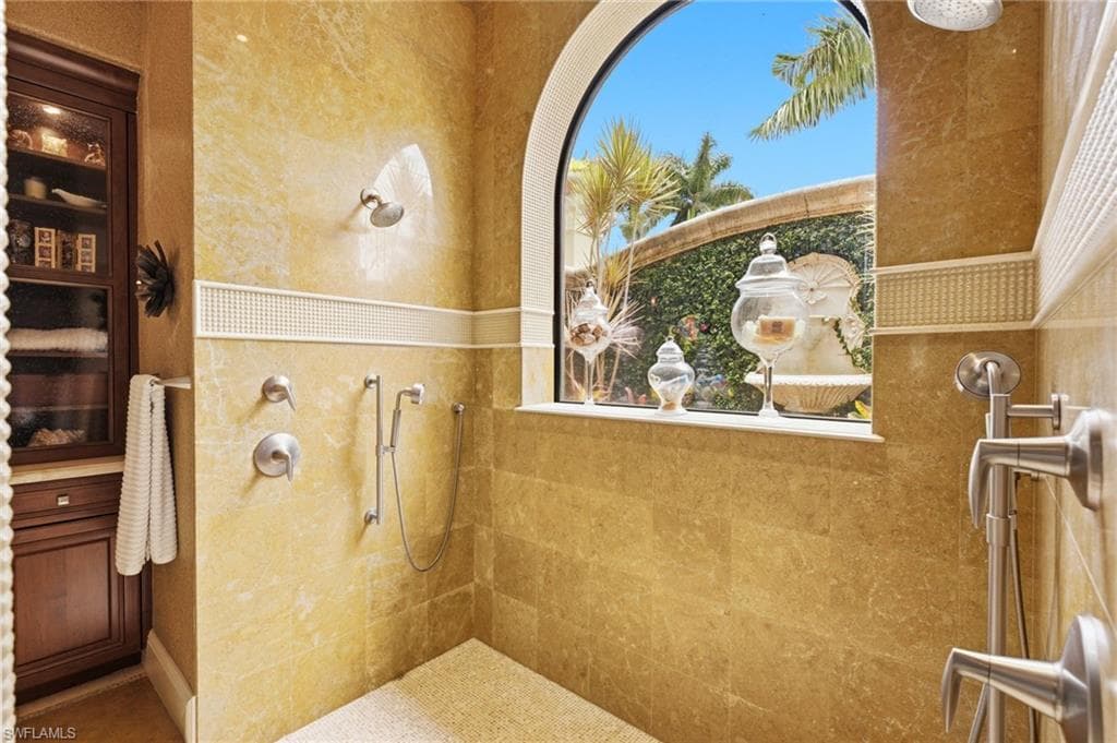 The expansive walk-through shower is a true spa experience, featuring a private window that frames a tranquil water feature while filling the space with abundant natural light, creating a serene and rejuvenating atmosphere.
