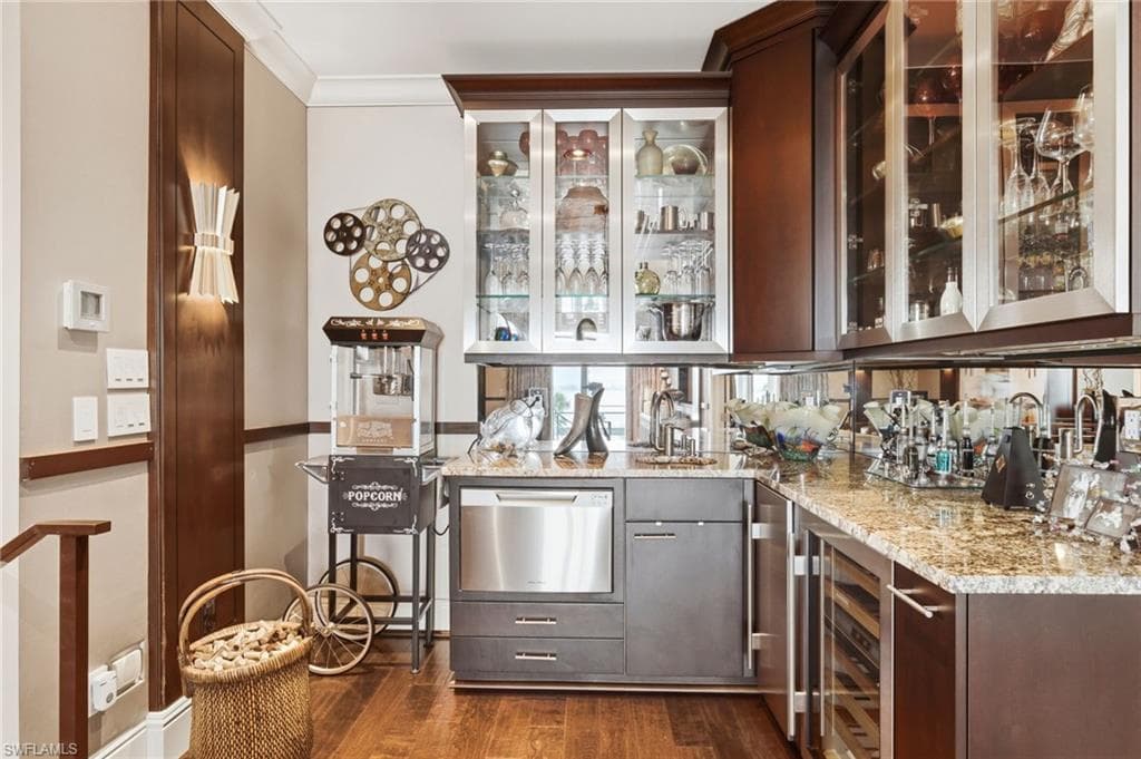 The second-level theater room is elevated by a sophisticated entertainment kitchen featuring a dishwasher, wine cooler, ice maker, beautiful glass-front cabinetry, a classic popcorn machine, and a striking mirrored backsplash—creating the ultimate setting for relaxed movie nights and effortless entertaining.