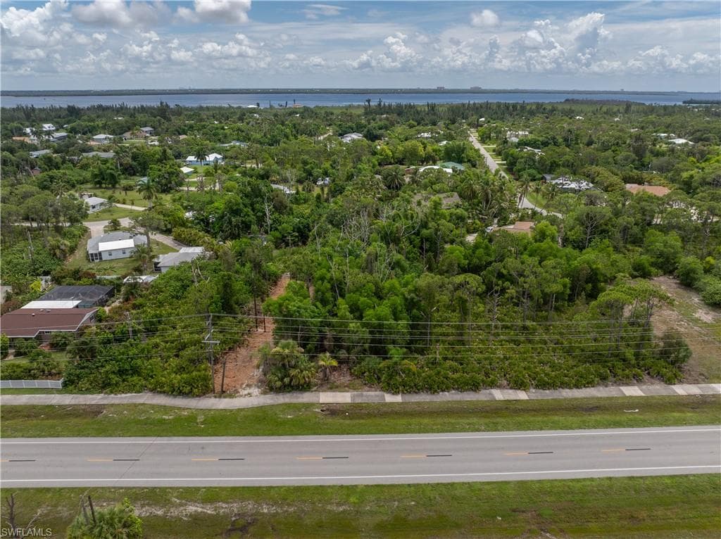Expansive lot with direct road frontage and mature trees, featuring a distant water backdrop