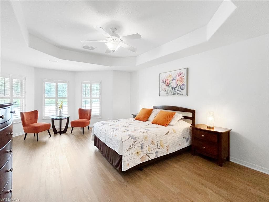 Tray ceiling with a ceiling fan, wood-finish flooring, and multiple windows with plantation shutters