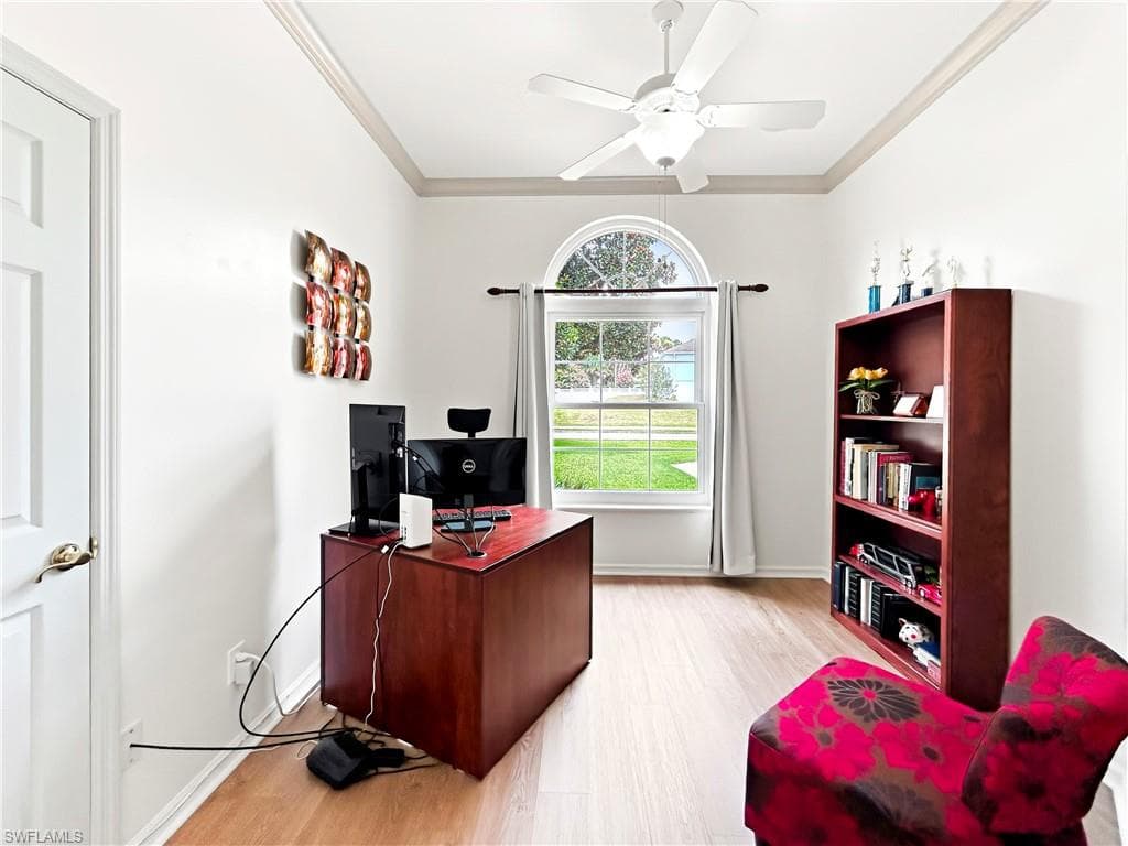 Wood-finish flooring, white paneled door, crown molding, arched window, and ceiling fan