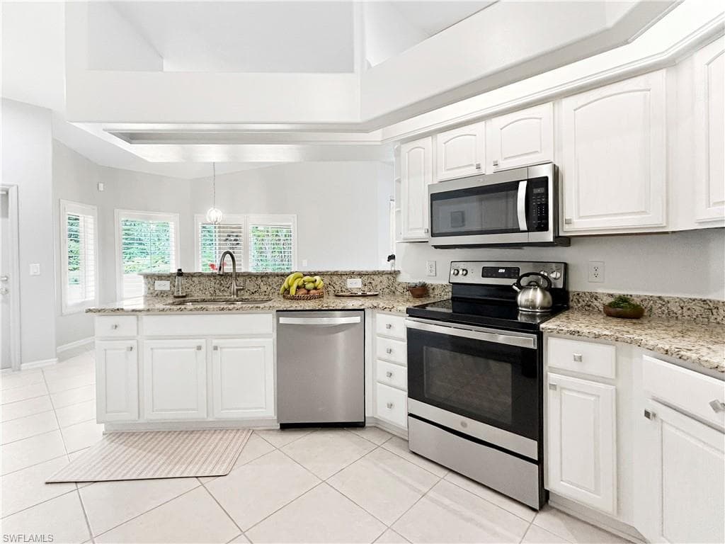 Kitchen featuring white cabinetry, light-toned tile flooring, stainless steel appliances, speckled stone countertops, and a vaulted ceiling
