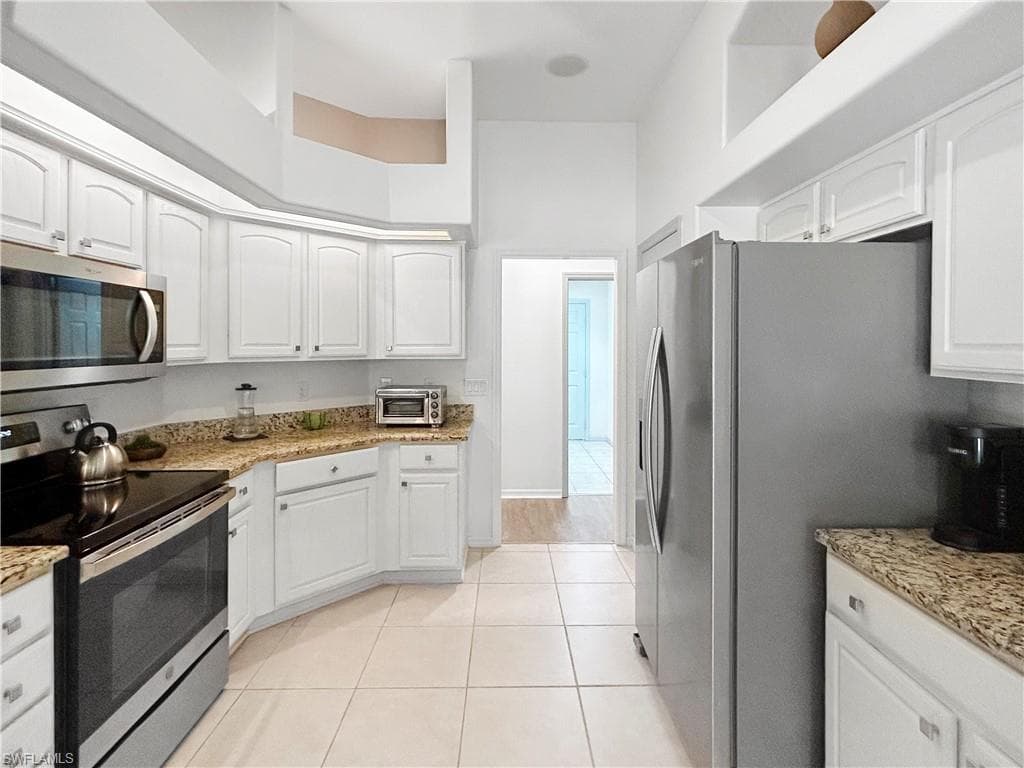Kitchen featuring white cabinetry, stone-finish countertops, stainless steel appliances, and tile flooring