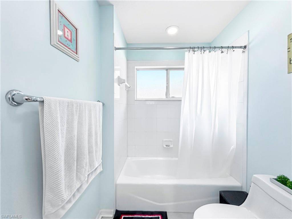 Bathtub with white tile surround, window, and chrome fixtures
