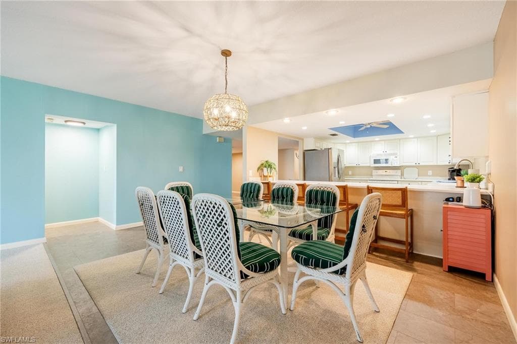 Dining area featuring a glass-top table, white wicker chairs with green striped cushions, and an overhead decorative light fixture