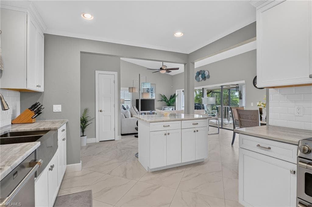 Open-concept kitchen featuring an island, white shaker cabinetry, light-toned countertops, tile flooring, and stainless steel appliances