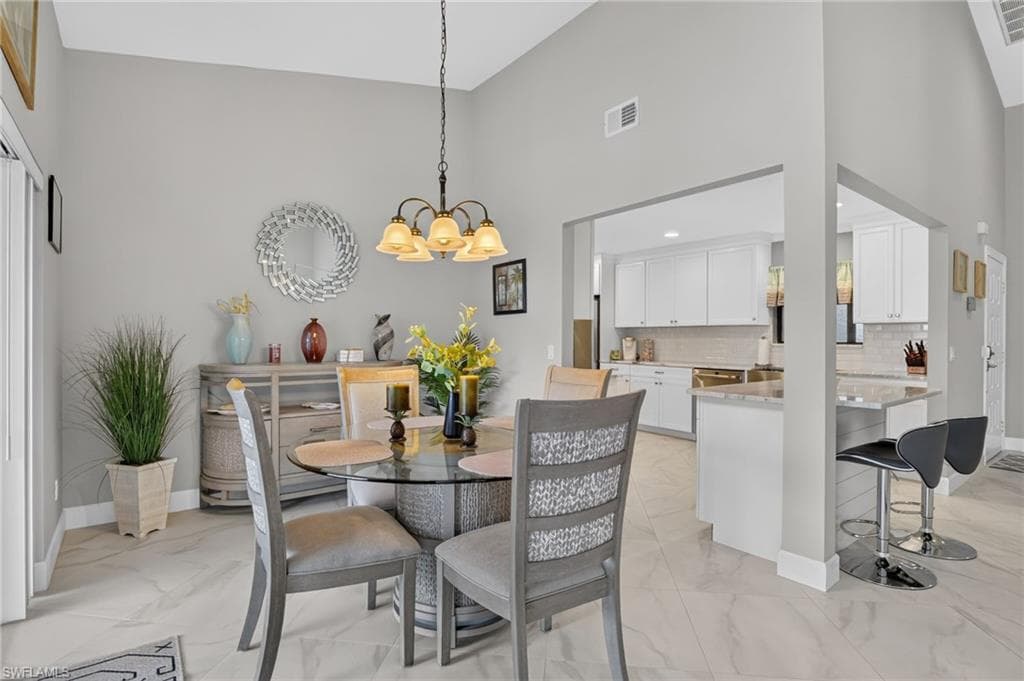 Vaulted ceiling dining area featuring a glass-top table, chandelier, and tile flooring