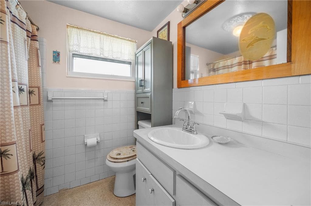 White tiled walls and flooring with a built-in vanity, integrated sink, and a framed mirror
