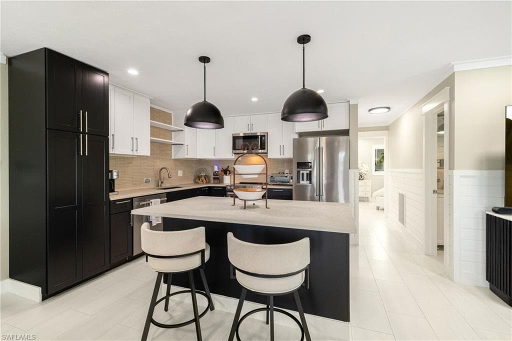 Kitchen featuring a two-tone cabinetry design, stainless steel appliances, pendant lighting, and a center island with countertop seating