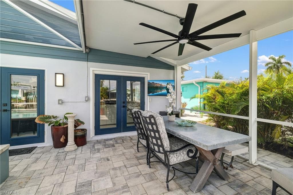 Screened outdoor living area featuring a large ceiling fan, paver flooring, and multiple glass-paneled exterior doors