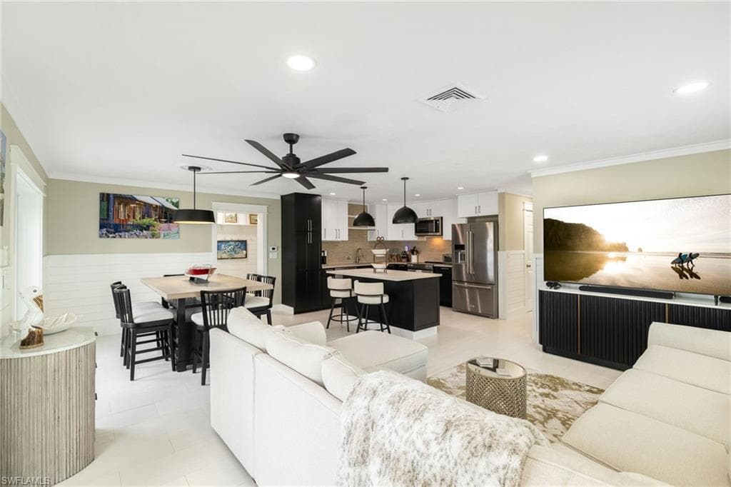 Open-concept living space featuring a central kitchen island with seating, stainless steel appliances, and a dining area with a linear pendant light
