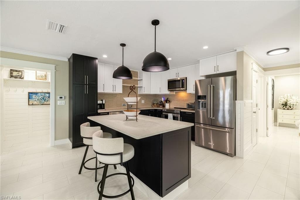Kitchen featuring a central island with countertop seating, stainless steel appliances, pendant lighting, and a neutral tile backsplash