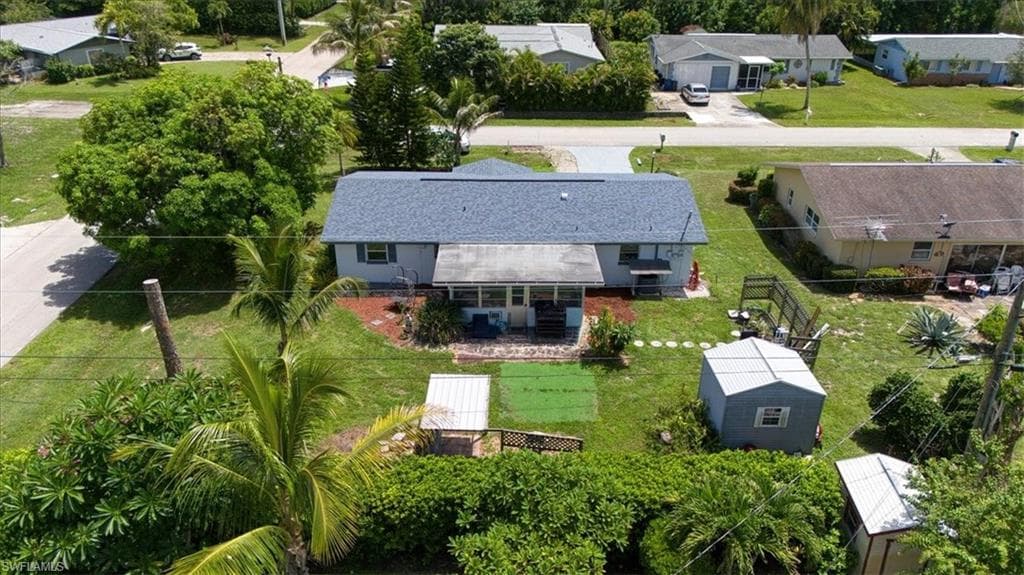 Single-story residence with a gray shingle roof, light-colored exterior, covered front porch, and a detached storage shed