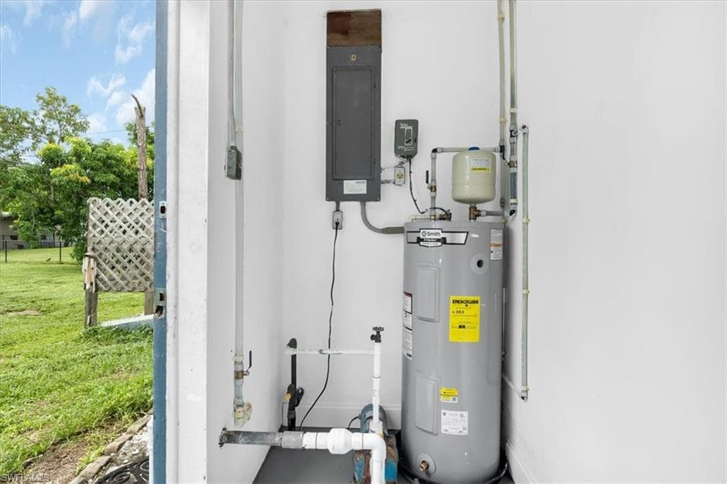Water heater with expansion tank and associated plumbing, electrical panel, and visible outdoor area with a white lattice fence