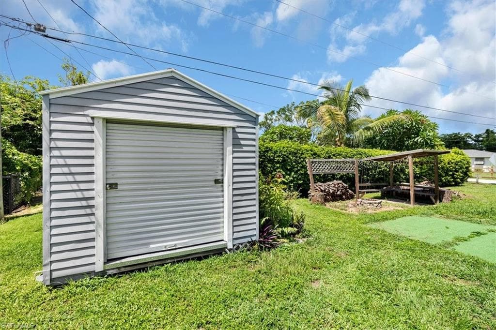 Detached storage shed with roll-up door, expansive green lawn, and privacy hedging