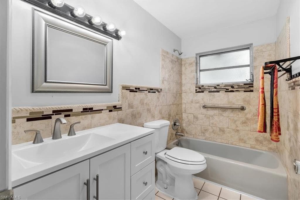 Dual-sink vanity with white cabinetry, tile flooring, and a tiled shower-tub combination