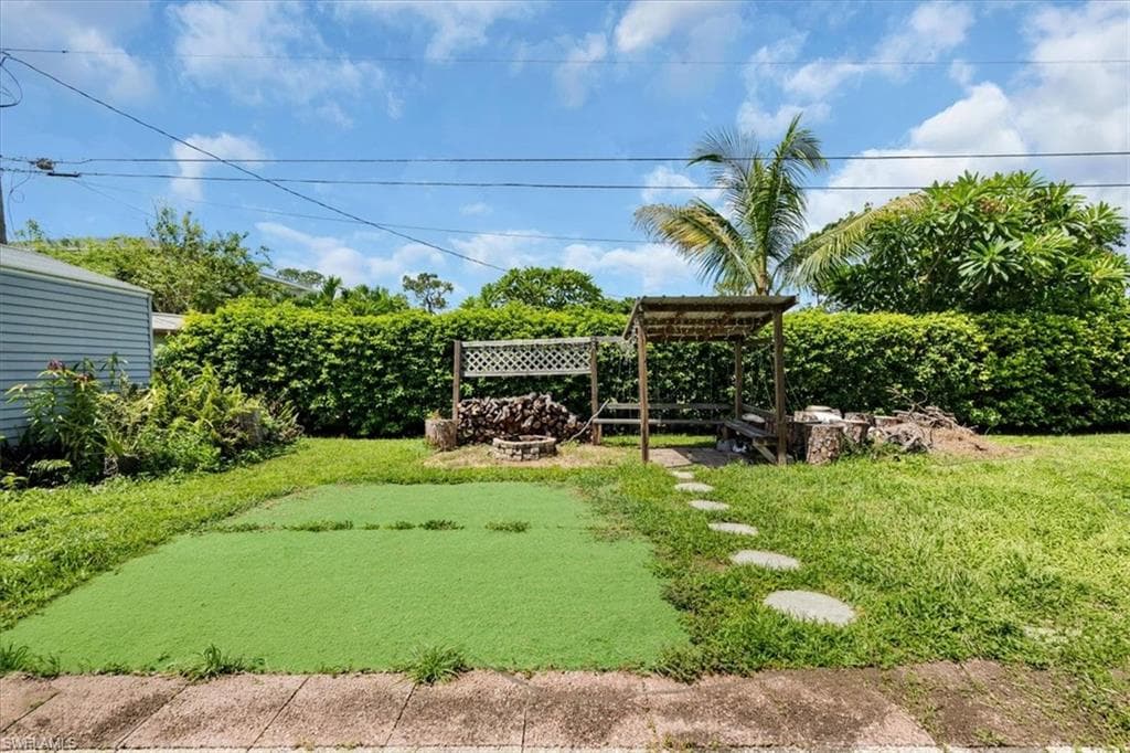 Fenced backyard featuring a gravel path, a covered pergola, and a fire pit area