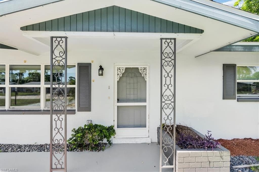 Covered entry with decorative metal support pillars, prominent front door with ornate security screen, exterior wall lantern, and a raised planter box