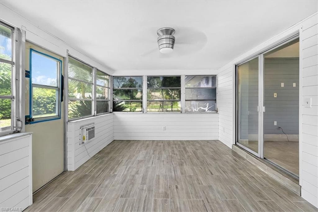 Enclosed patio featuring wood-finish flooring, white shiplap walls, multiple windows, a ceiling-mounted light fixture, and sliding glass doors