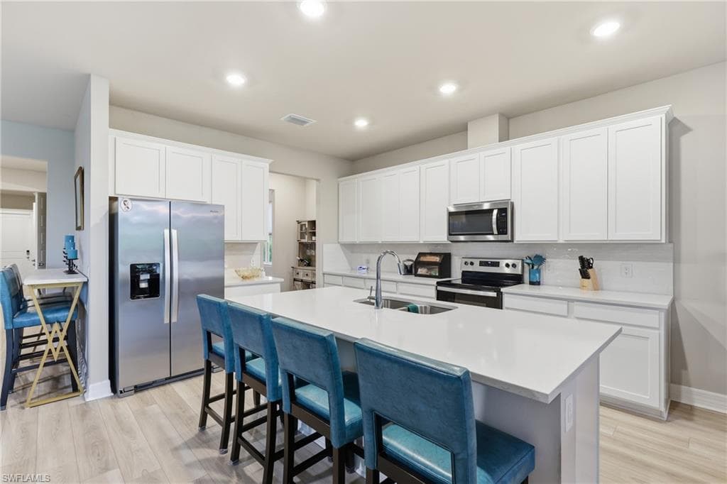 Bright, open Kitchen featuring quartz countertops, white cabinetry, stainless steel appliances, encompassing a large center island with seating, and abundant counter space, perfect for everyday living and entertaining