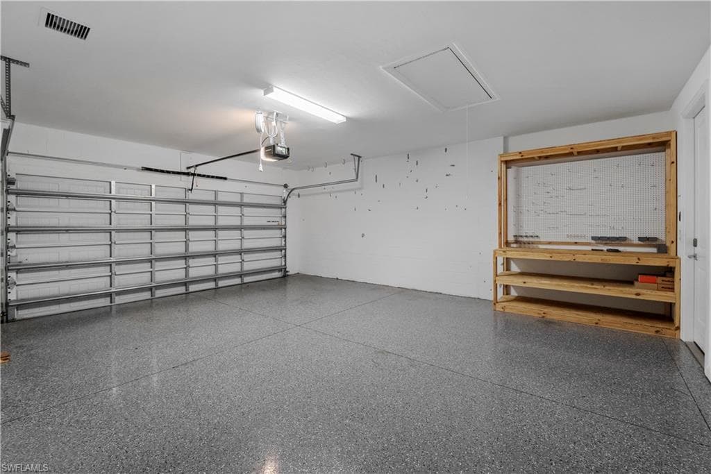 Attached garage featuring a patterned epoxy floor, automatic garage door opener, overhead lighting, and built-in shelving