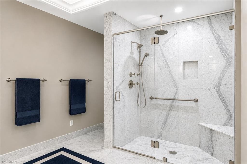 Glass-enclosed shower with a built-in bench, recessed niche, and stone tile surround