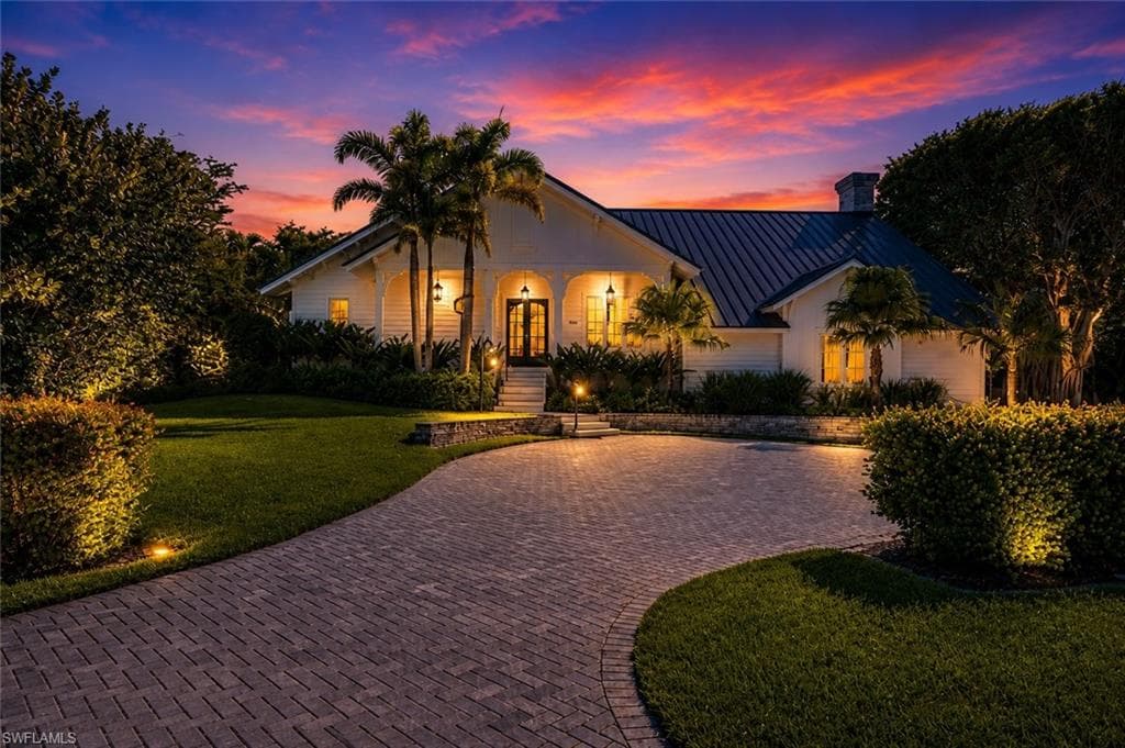 White exterior with a dark metal roof, a curved paver driveway, and professional landscaping