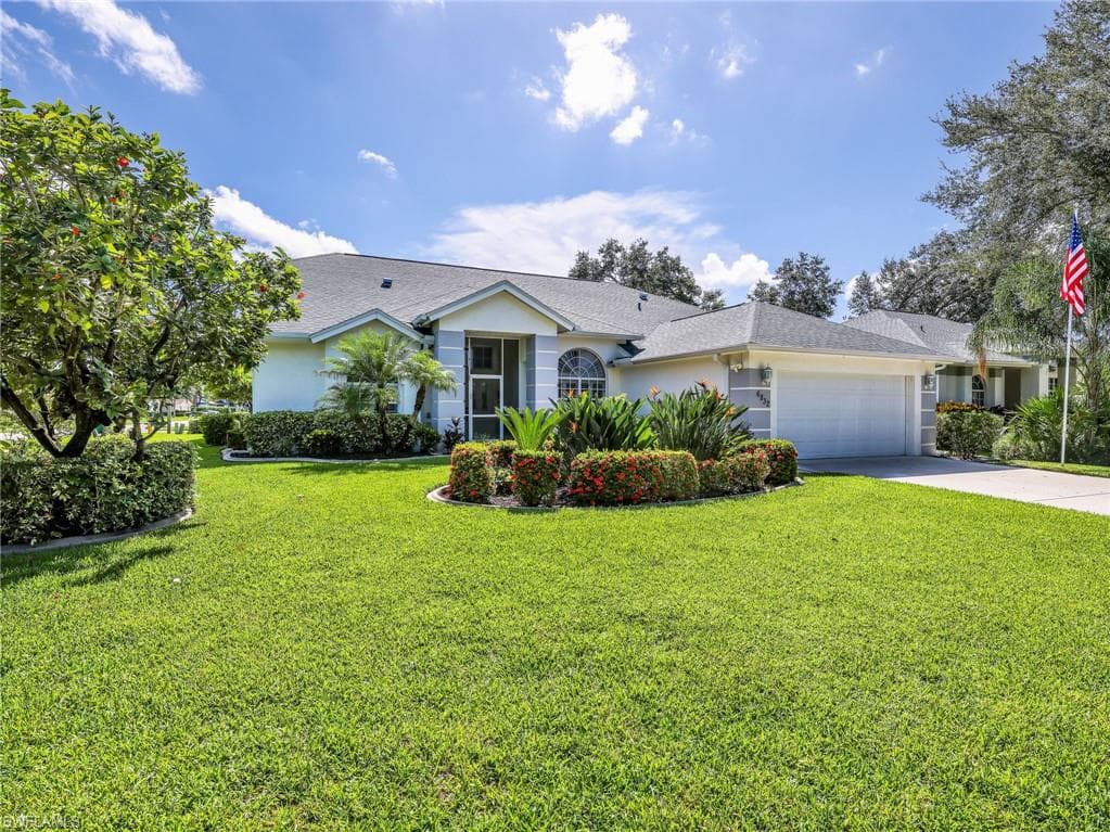 Manicured lawn with mature landscaping, attached two-car garage, paved driveway, and covered entry