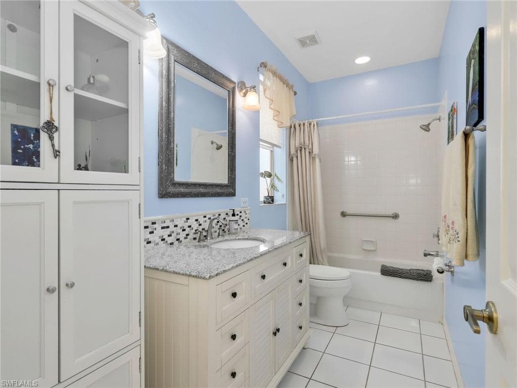 White tile flooring, white vanity with integrated sink, stone countertop, mosaic tile backsplash, and built-in white cabinetry with glass inserts