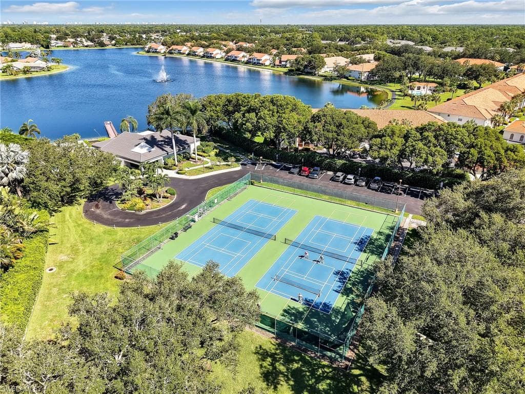 Multiple tennis courts, paved parking area, lush landscaping, and a water feature