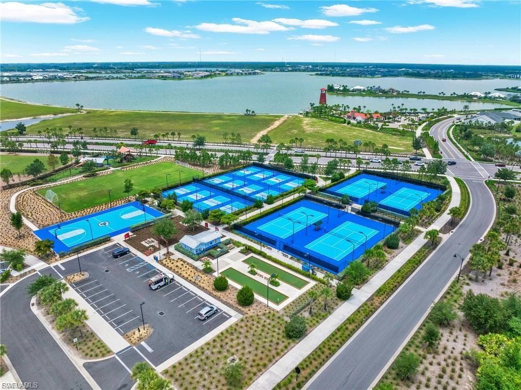 Expansive recreational complex featuring multiple tennis courts, a basketball court, an open field, and a putting green, all situated by a large body of water
