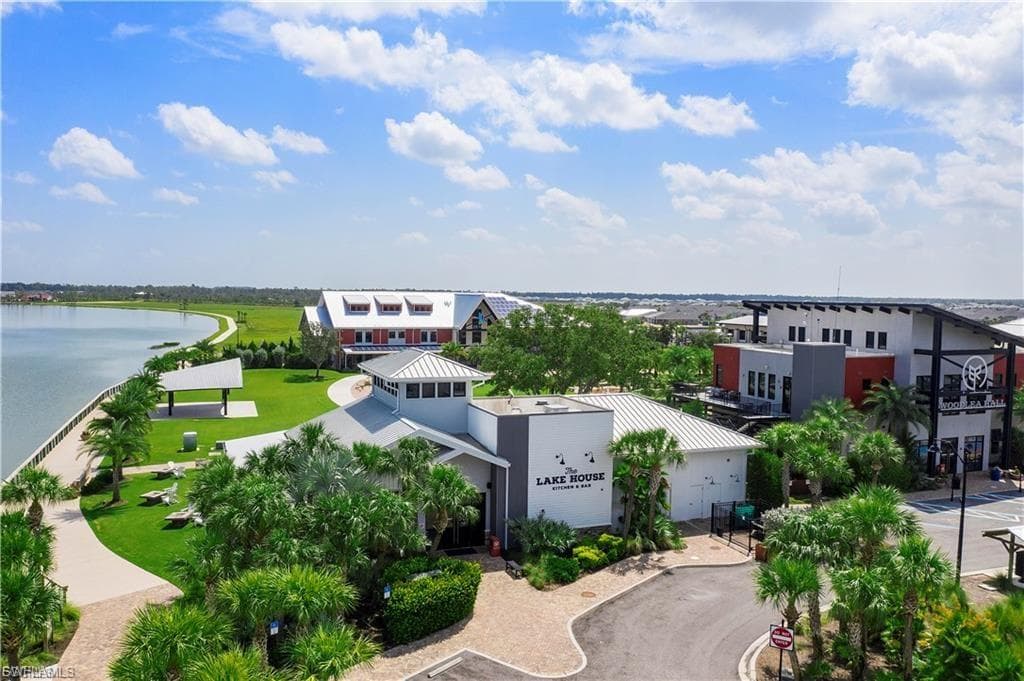 Waterfront property featuring modern mixed-use architecture with multiple buildings, expansive manicured grounds with mature palmettos and landscaped grounds, waterfront promenade with curved pathways, and panoramic water views across the property