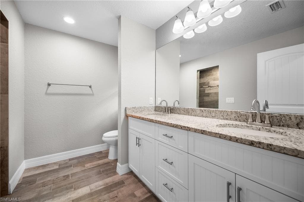 Dual vanity with stone countertop and undermount sinks, wood-finish flooring, white cabinetry, and recessed lighting