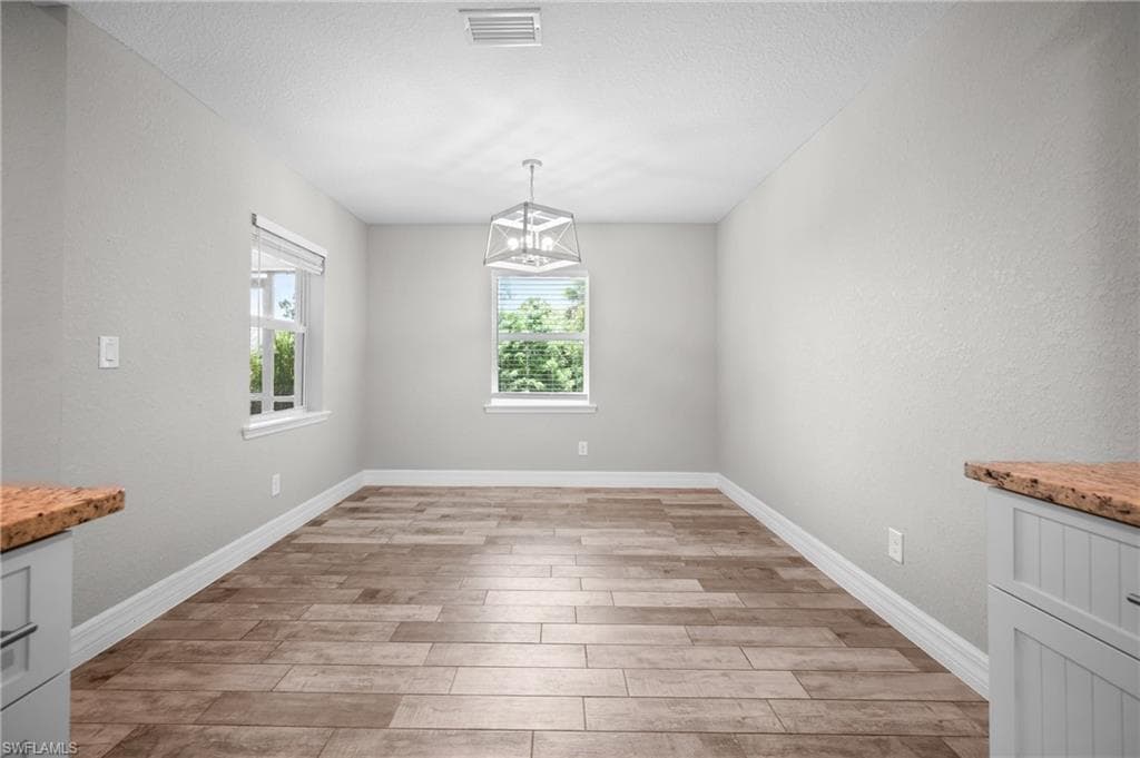 Bright, open room featuring wood-finish plank flooring, clean white walls, and abundant natural light from dual windows