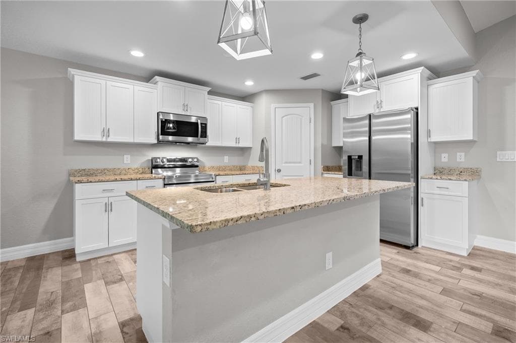 Kitchen featuring wood-finish flooring, white cabinetry, a central island with a sink, stainless steel appliances, and recessed lighting