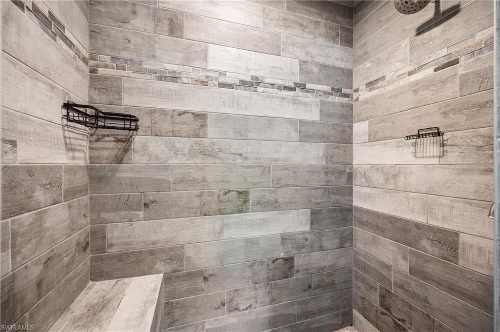 Shower stall featuring wood-finish wall tile, a decorative mosaic tile accent band, and a built-in shower bench