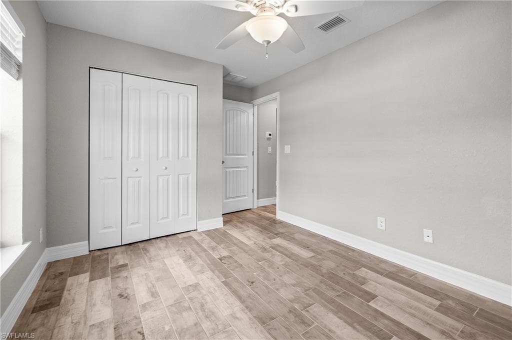 Wood-finish flooring, white bi-fold closet doors, ceiling fan, and light gray wall paint