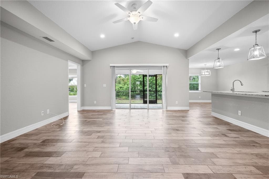 Vaulted ceiling with a ceiling fan and recessed lighting, wood-finish flooring, sliding glass doors, and a kitchen island with pendant lighting and a stainless steel faucet