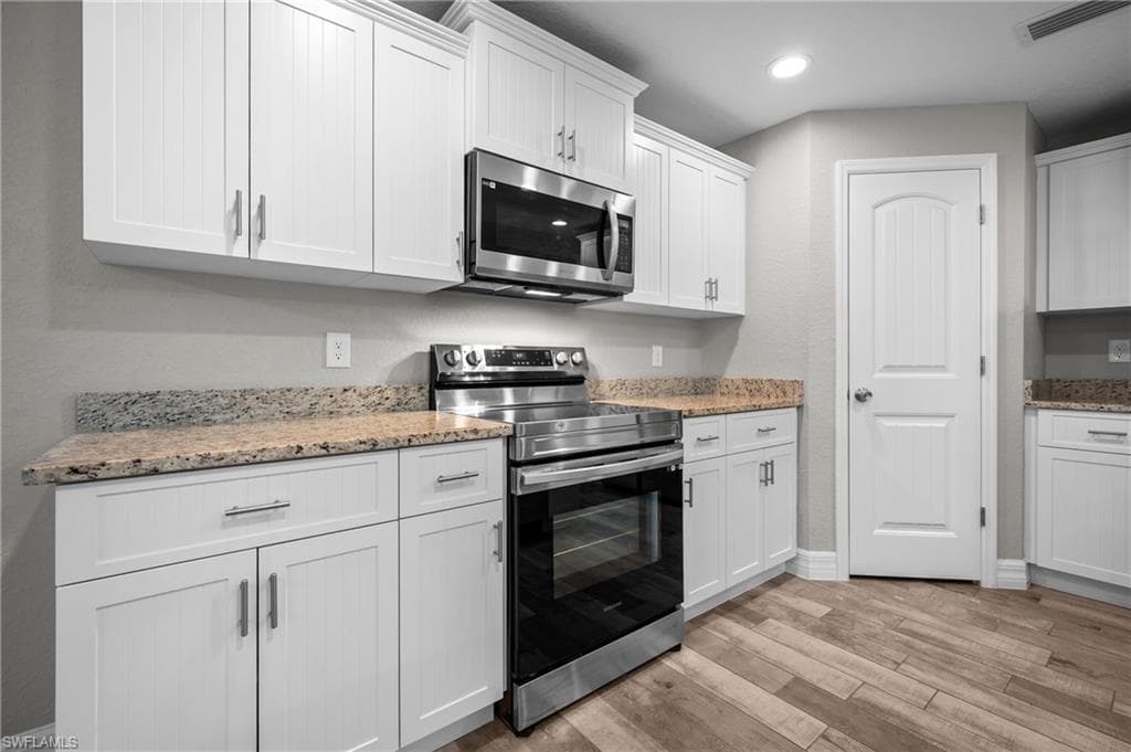 White cabinetry with brushed nickel hardware, stainless steel appliances, granite countertops, and wood-finish plank flooring