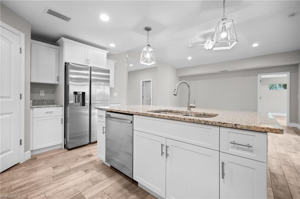 Kitchen featuring white shaker cabinetry, stainless steel appliances, granite countertops, wood-finish flooring, and pendant lighting