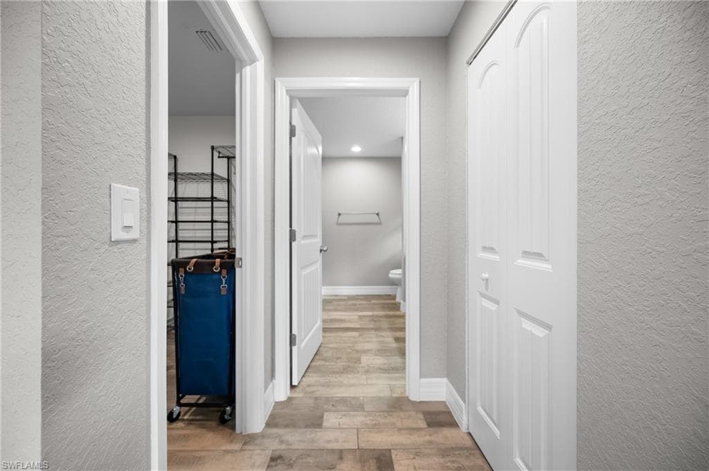Hallway featuring wood-finish flooring, white paneled doors, and light gray wall texture
