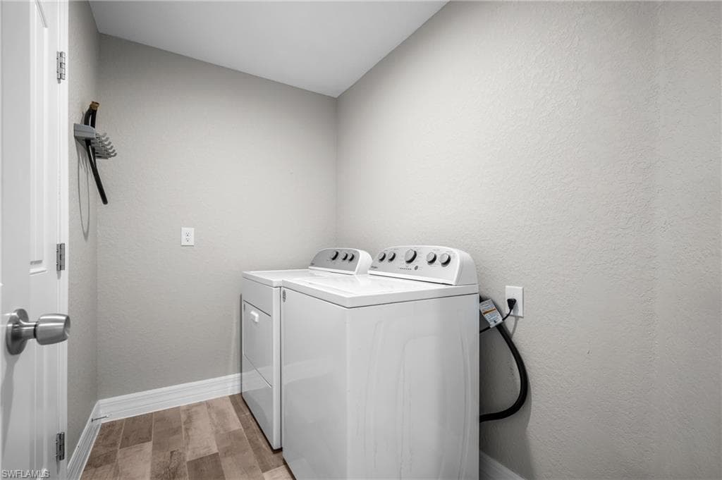 Dedicated laundry room featuring a top-load washer with multiple wash cycles, matching white cabinetry, wood-finish flooring, neutral wall finishes, and a wall-mounted utility hook for storage and organization
