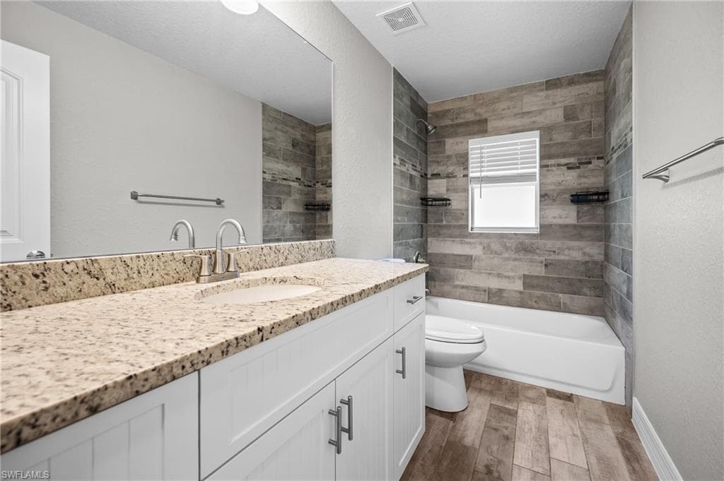 Modern bathroom featuring dual vanity with stone-finish countertop and white cabinetry, walk-in shower with wood-finish tile surround and frameless glass enclosure, wood-finish plank flooring, and large window with horizontal blinds