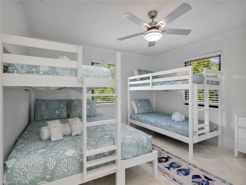Bright room featuring two white bunk beds, a ceiling fan with integrated lighting, and multiple windows with horizontal blinds