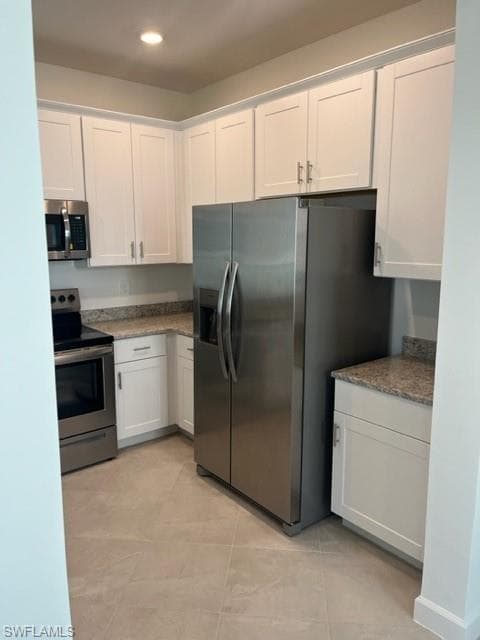Kitchen featuring stove, stainless steel fridge with ice dispenser, white cabinets, recessed lighting, and light tile patterned floors