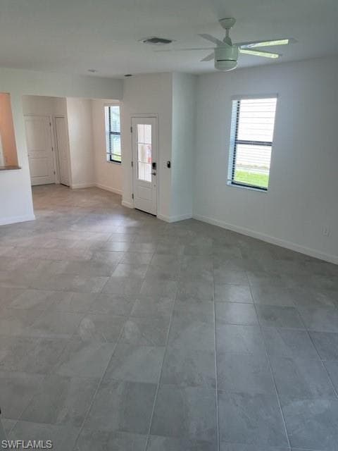 Tiled spare room featuring a ceiling fan and baseboards
