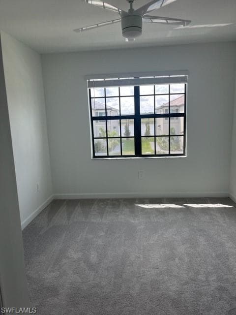 Spare room featuring a ceiling fan, healthy amount of natural light, dark carpet, and baseboards