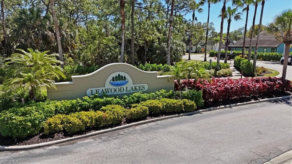 Leawood Lakes community entrance featuring an elegant arched monument sign, lush tropical landscaping with mature palms and flowering shrubs, and manicured hedges lining a paved driveway approach